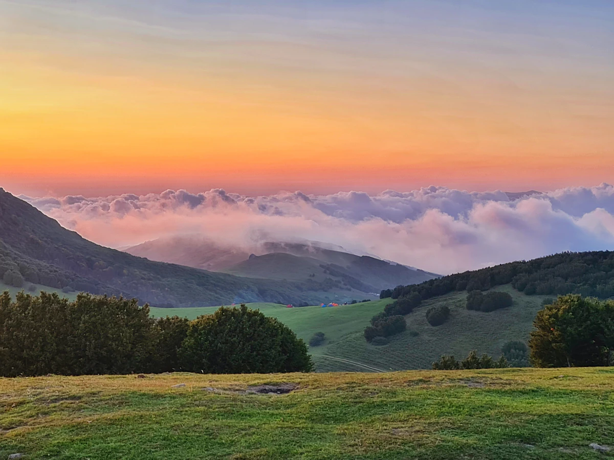 a mountain covered in green grass next to a lush green hillside